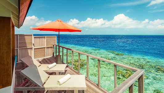 Två solstolar med vita handdukar på en träterrass bredvid havet, med ett parasoll. (AI-genererad text)