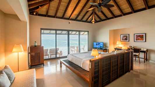 Interiör av ett sovrum med en dubbelsäng och ett öppet fönster mot en balkong. (AI-genererad text)