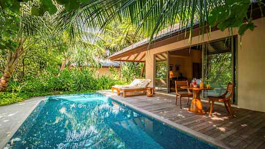 En privat pool vid en tropisk villa med en solstol och ett bord med stolar. (AI-genererad text)