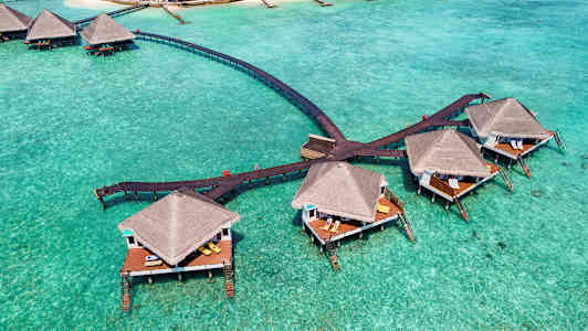 Bungalows på pålar över turkost vatten, anslutna med träbroar. (AI-genererad text)