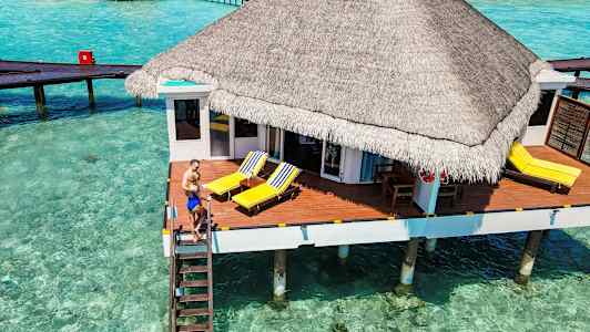 Bungalow på pelare över klart turkost vatten med soldäck och strandstolar. (AI-genererad text)