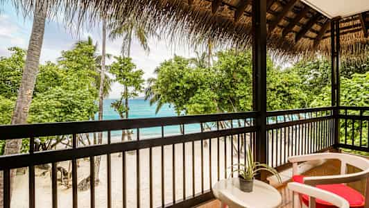 Utsikt från en terrass mot en sandstrand med palmer och hav. (AI-genererad text)