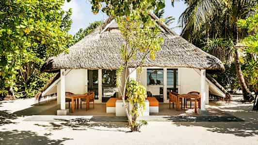 En bungalow med halmtak, omgiven av träd och växtlighet, med havsutsikt i bakgrunden. (AI-genererad text)