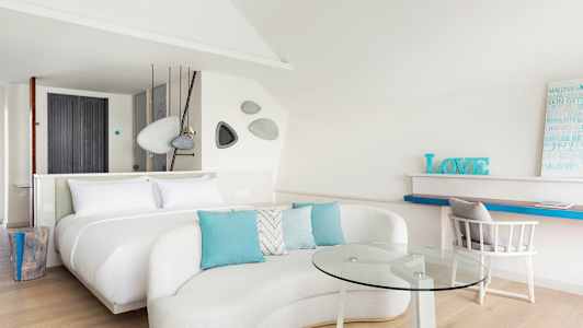 Ett modernt och ljust hotellrum med en stor säng, soffgrupp med glasbord, och arbetsplats. (AI-genererad text)