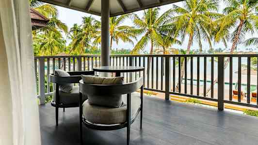 Bild av en utomhusterrass med två grå sittmöbler och ett bord. Terrassen har utsikt över palmer och en strand. (AI-genererad text)