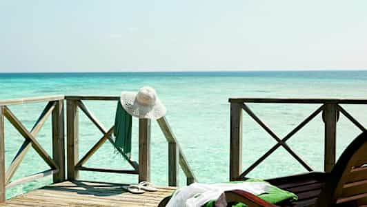 Träterrass vid havet med ett vitt solhatt och ett grönt klädesplagg hängande på räcket. (AI-genererad text)