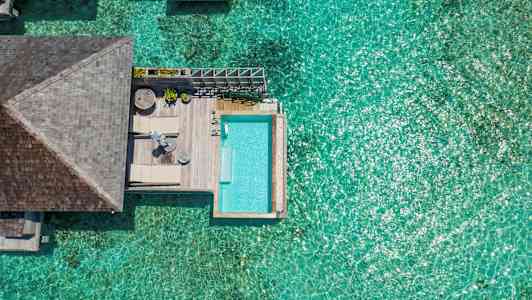 Vy från ovan av ett soligt vattenvillorområde med en pool och klarblått hav. (AI-genererad text)