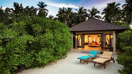 Bungalow framför grönska med solstolar på sand. (AI-genererad text)