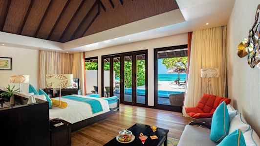 Ett rymligt rum med säng, sittplatser och utsikt över en pool samt havet genom stora fönster. (AI-genererad text)