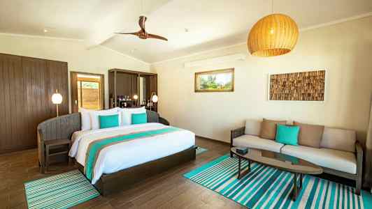 Ett ljust rum med en dubbelsäng, en soffa, och ett soffbord, dekorerat i turkosa och neutrala färger. (AI-genererad text)