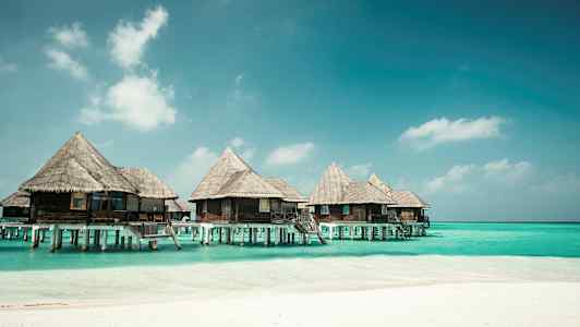 Bungalows på pålar över blått vatten vid en strand. (AI-genererad text)