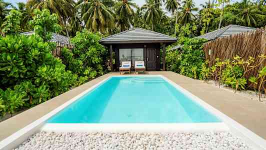En swimmingpool med utsikt mot en tropisk bungalow och omgivande växtlighet. (AI-genererad text)