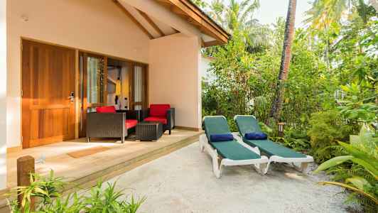 En uteplats med två solstolar och sittgrupp framför en byggnad omgivet av grönska. (AI-genererad text)