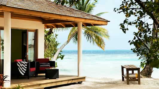 Strandvilla med veranda möblerad med soffor, bord och dekorerad med palmer runtom. (AI-genererad text)