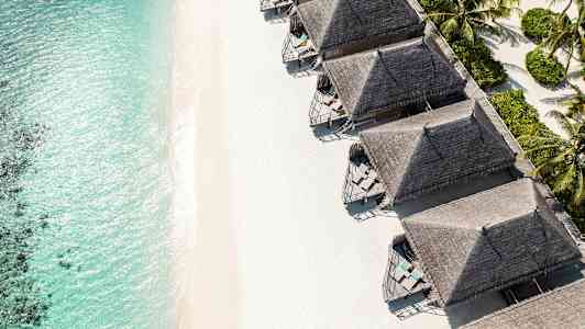 Strand med turkost vatten och flera strandnära bungalows. (AI-genererad text)