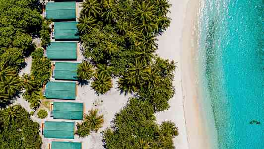 Flygbild av grönskande träd, byggnader med grönt tak och stranden vid turkost hav. (AI-genererad text)