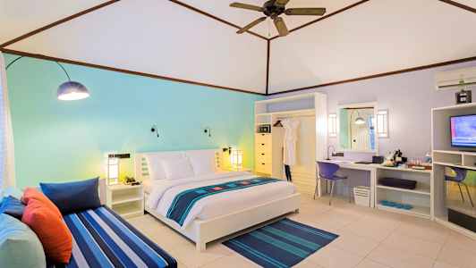 Ett ljust hotellrum med en dubbelsäng, färgstarka dekorationer och en sittgrupp. (AI-genererad text)