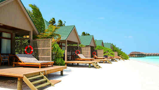 Strandbungalower med grön tak och solstolar vid vattnet. (AI-genererad text)