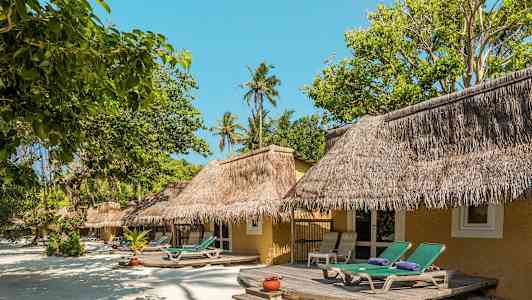Strandbungalow med halmtak och solstolar framför omgiven av grönska. (AI-genererad text)