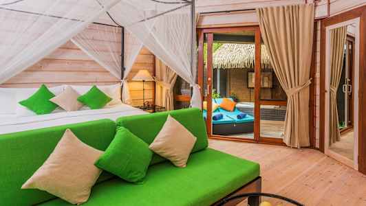 Ett sovrum med en grön soffa och en säng med gröntonade prydnadskuddar. Till höger finns en glasdörr som leder till en uteplats med solstolar. (AI-genererad text)