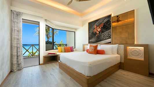 Ett modernt hotellrum med en stor säng, färgglada kuddar, rymliga fönster och utsikt över havet. (AI-genererad text)