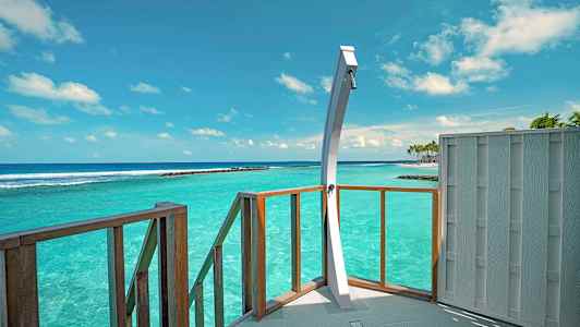 En dusch på en altan med utsikt över turkost hav under en klar himmel. (AI-genererad text)