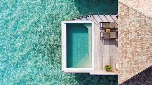 En ovanifrån bild av ett poolområde med trädäck vid vattnet. (AI-genererad text)