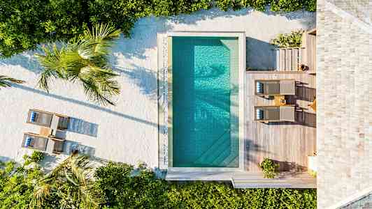 Luftbild av en pool med omgivande trädäck, solstolar och växter. (AI-genererad text)