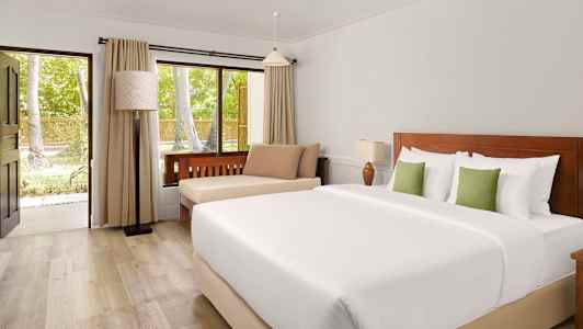 Ett hotellrum med en dubbelsäng, sittplats och ett fönster som vetter mot gröna träd. (AI-genererad text)