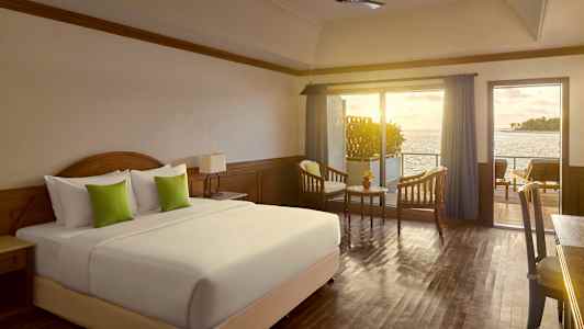 Ett hotellrum med en stor säng, två fåtöljer och ett bord framför en balkong med havsutsikt. (AI-genererad text)