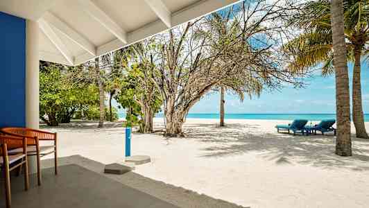 En sandstrand med några solstolar, palmer och ett blått hav i bakgrunden, sedd från en uteplats. (AI-genererad text)