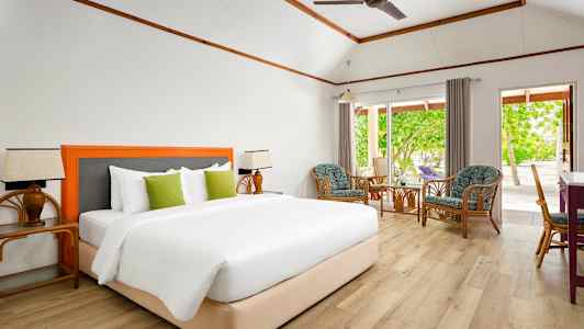 Ett rum med en bekväm dubbelsäng, sittgrupp med stolar och ett bord, och stora fönster som erbjuder utsikt mot en grönskande trädgård. (AI-genererad text)