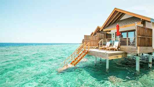 Fotografi av en bungalow på pålar över turkost vatten. (AI-genererad text)