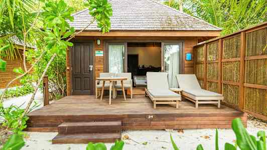 En bungalow med träfasad, terrass med solstolar och bord, omgiven av grönska. (AI-genererad text)