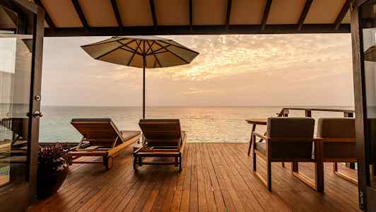 En terrass med solstolar och parasoll vetter mot havet vid solnedgång. (AI-genererad text)