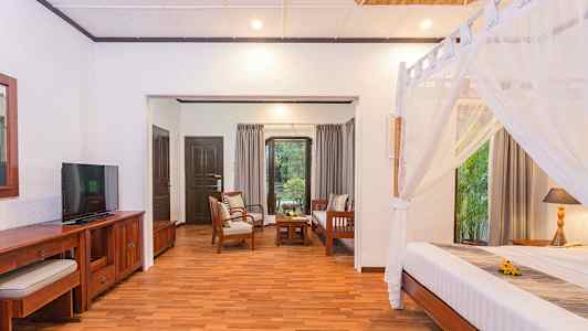 Ett rum med trämöbler, en säng med myggnät och en sittgrupp med utsikt mot en trädgård. (AI-genererad text)