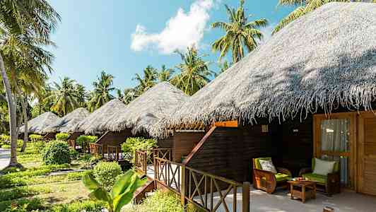 Bilden visar flera bungalows med halmtak omgivna av tropiska växter och palmer. (AI-genererad text)