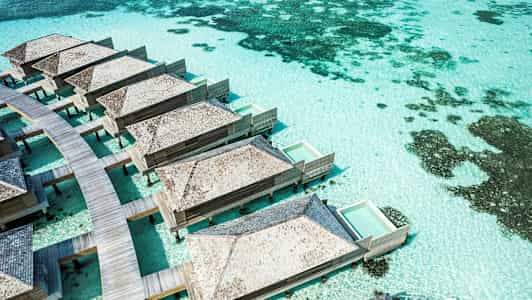 Bungalows på pålar med privata pooler över turkost vatten. (AI-genererad text)