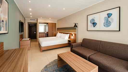 Ett hotellrum med en dubbelsäng, soffa, bord och väggkonst. (AI-genererad text)