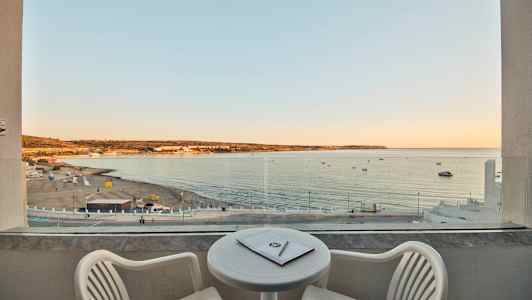 Utsikt från en balkong över en sandstrand och havet vid solnedgången. (AI-genererad text)