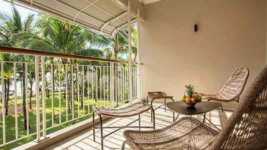 En möblerad balkong med utsikt över en trädgård med palmer. (AI-genererad text)