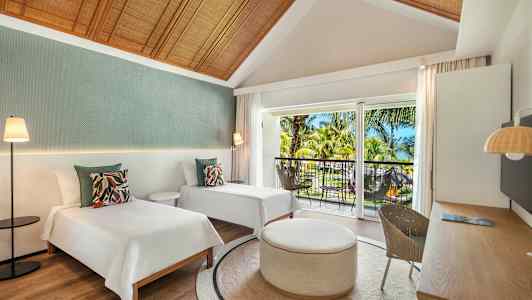 Ett hotellrum med två enkelsängar, ett runt bord och en balkong med utsikt över tropiska träd. (AI-genererad text)