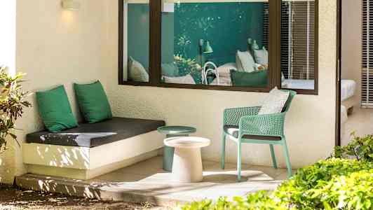 Utomhus sittplats med grön inredning och utsikt mot sovrumsinteriör. (AI-genererad text)