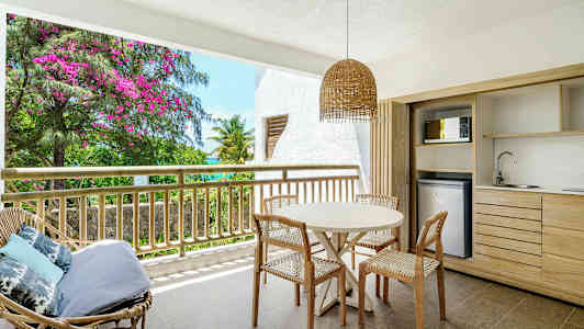 En terrass med bord och stolar, samt en utsikt mot grönska och blommor. (AI-genererad text)