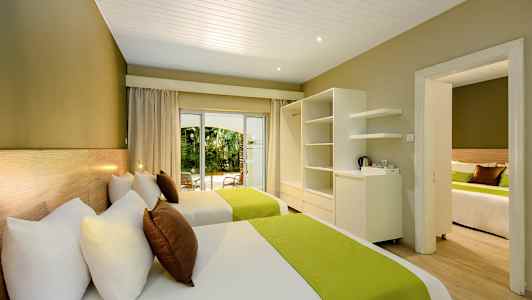 Hotellrum med två sängar, gröna sängöverkast och utsikt mot trädgården. (AI-genererad text)