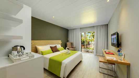 Hotellrum med dubbelsäng, skrivbord och balkong med utsikt över träd och grönska. (AI-genererad text)