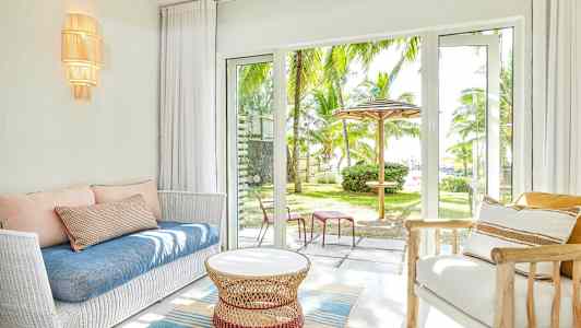 Vardagsrum med vit soffa, blå kudde och glasdörrar som öppnar mot en trädgård med palmträd. (AI-genererad text)