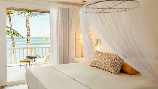 En ljus hotellsvit med en himmelssäng och utsikt över havet från balkongen. (AI-genererad text)