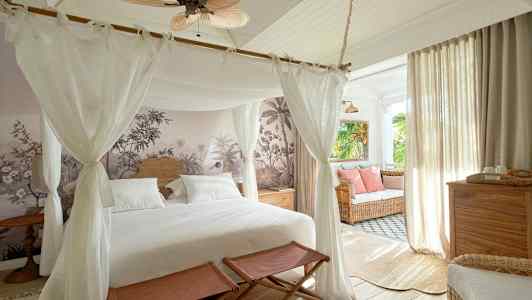 Ett sovrum med himmelssäng, väggdekoration och inredning med ljusa möbler samt en sittgrupp vid fönstret. (AI-genererad text)