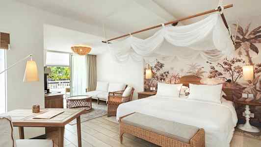 Ett ljust sovrum och vardagsrum med sängar, sittmöbler och tropiska dekorationer. (AI-genererad text)